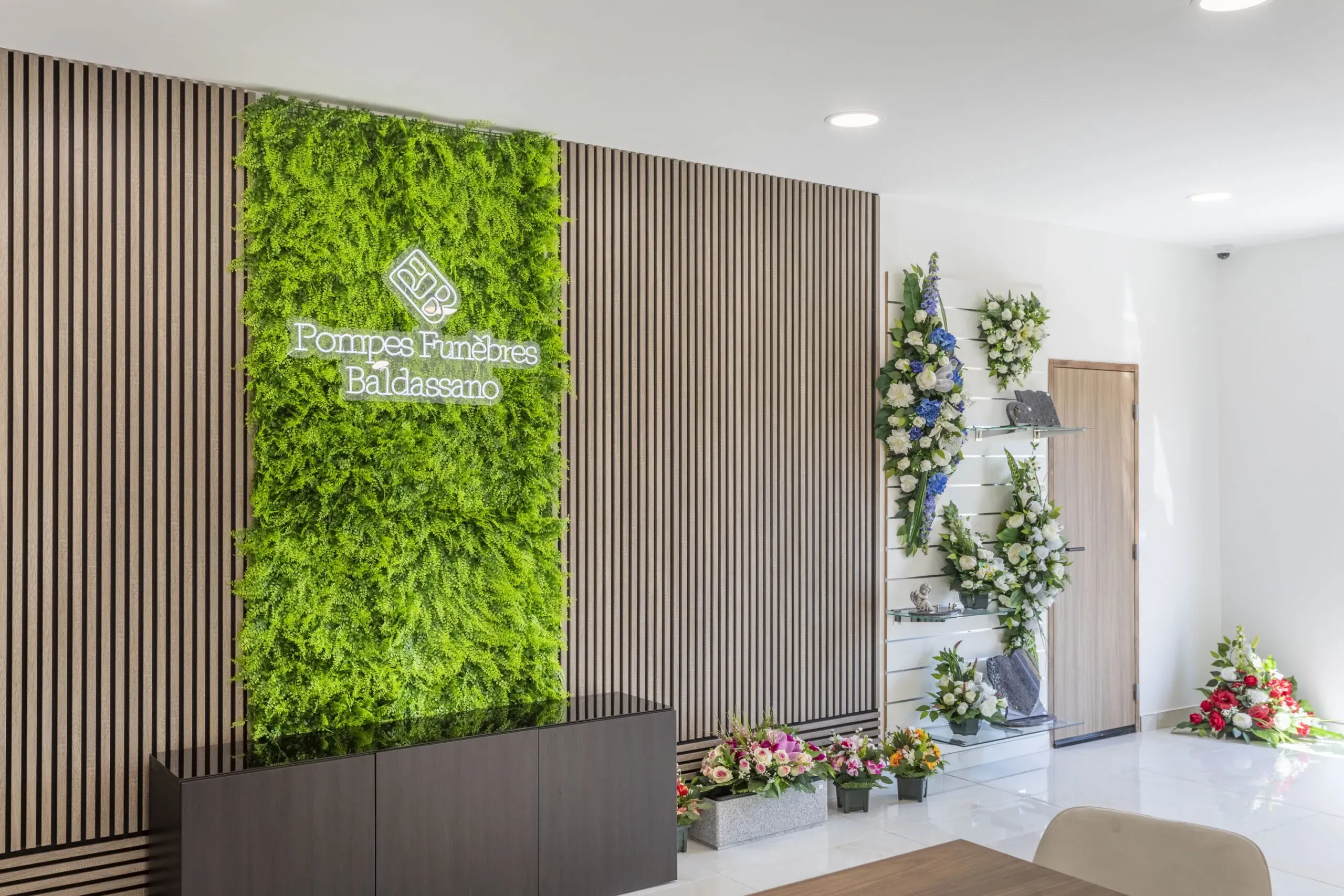 Intérieur moderne de l'agence Pompes Funèbres Baldassano avec mur végétal et fleurs.